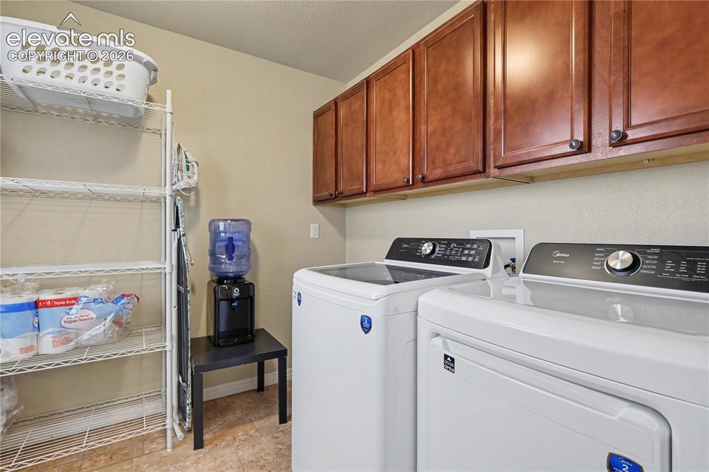 Image 14 of 38: Dedicated laundry area featuring upper wood-finish cabinetry, a textured ti