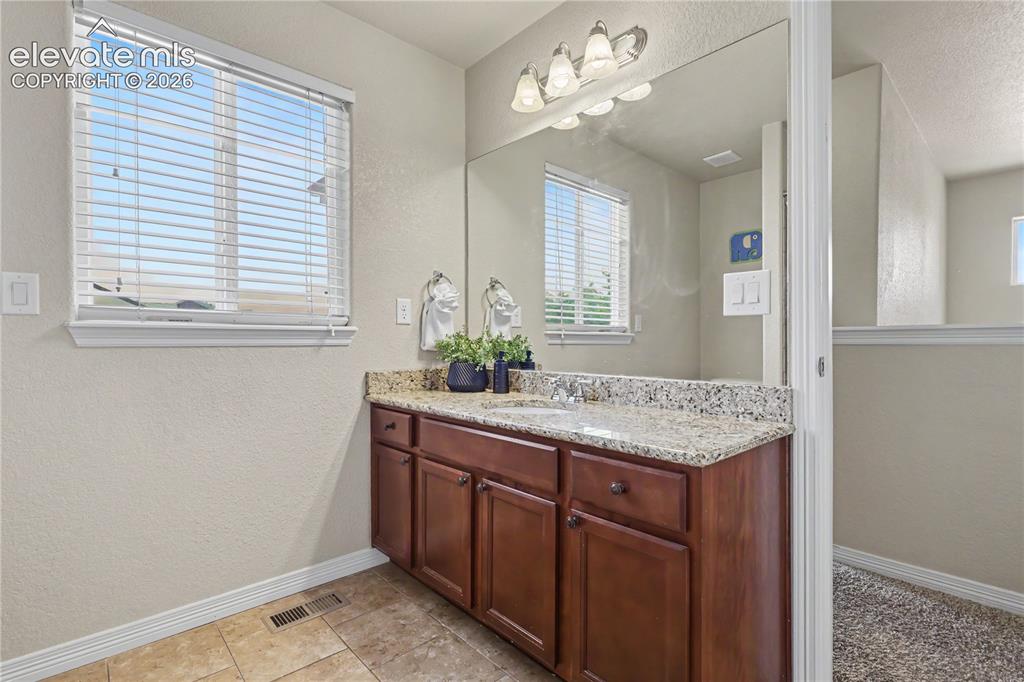 Image 26 of 38: Bathroom vanity with a granite-style countertop, undermount sink, and wood-