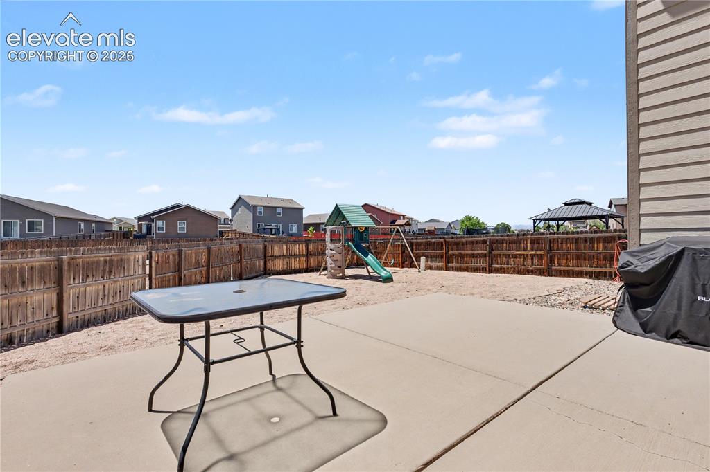 Image 36 of 38: Concrete patio area with a wooden privacy fence, gravel landscaping, and a