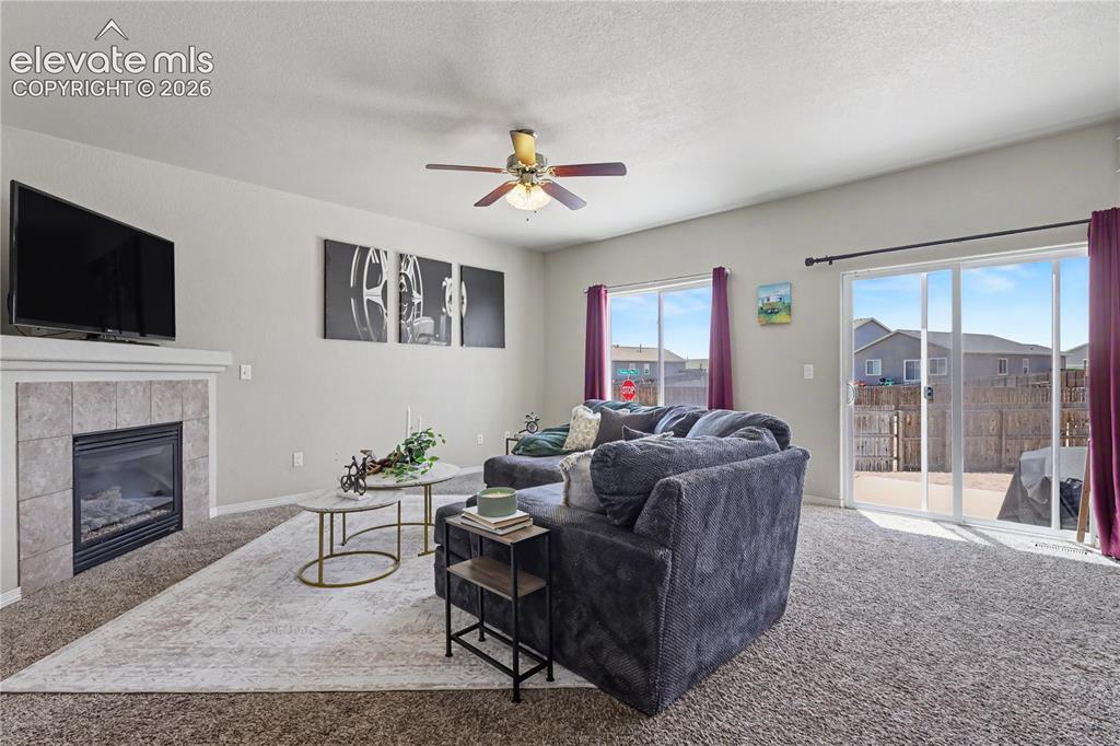 Image 5 of 38: Living area featuring a gas fireplace with a tiled surround, a ceiling fan,