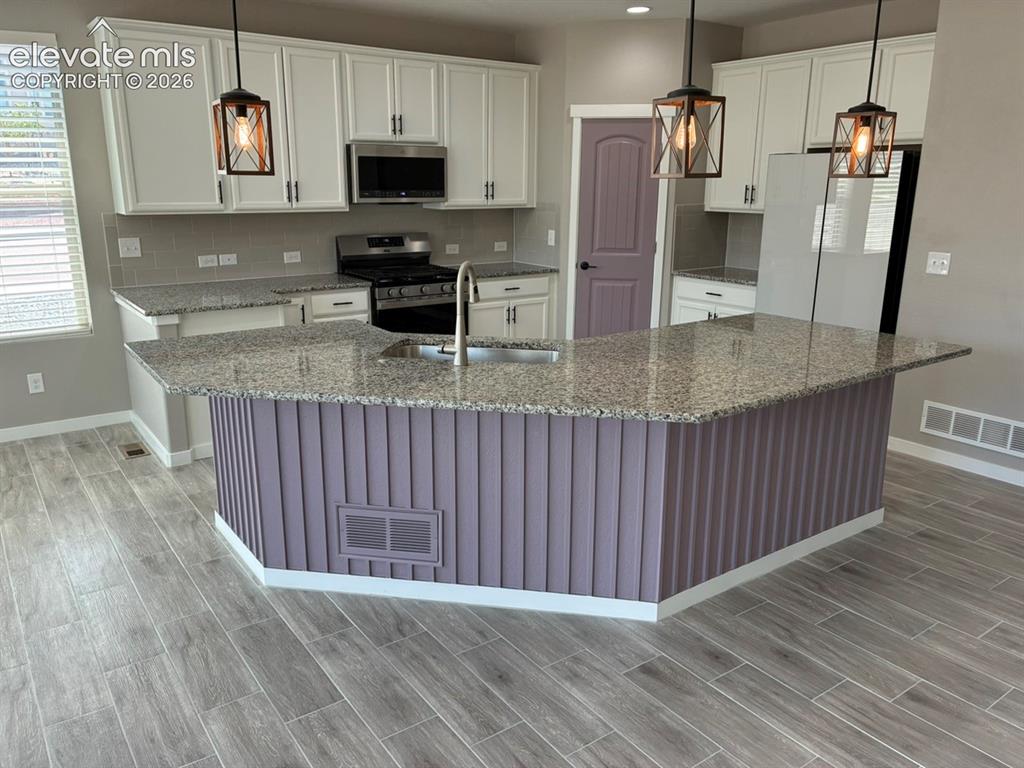 Image 12 of 48: Kitchen featuring a large island with sink, white shaker cabinetry, stainle