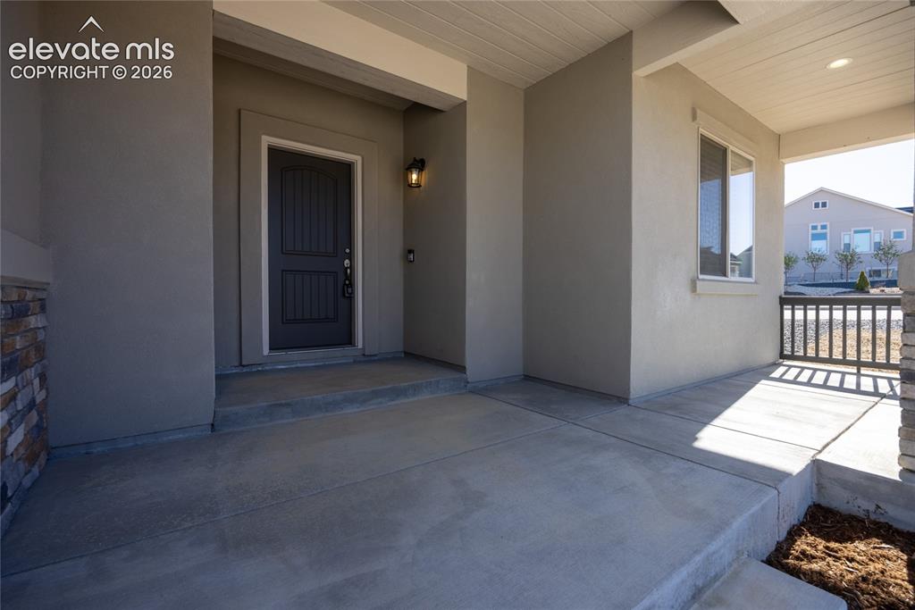 Image 16 of 48: Covered front porch with concrete flooring, stone-clad column, dark paneled