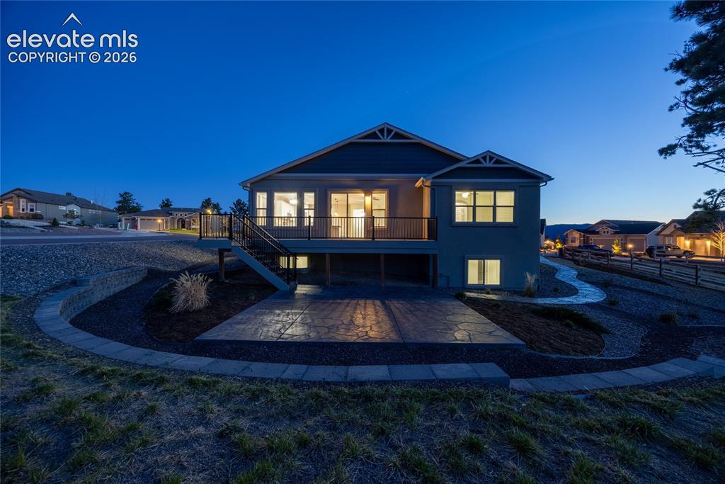 Image 4 of 48: Elevated deck with dark railings, concrete patio, stone retaining wall, and