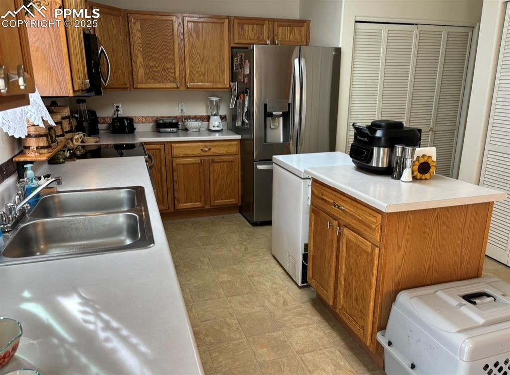 Image 6 of 15: Kitchen with brown cabinetry, stainless steel appliances, light countertops