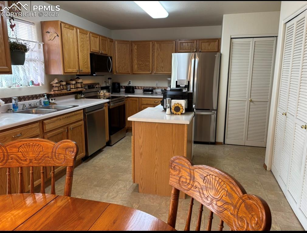 Image 8 of 15: Kitchen with brown cabinetry, stainless steel appliances, light countertops