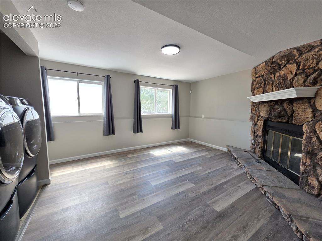 Image 13 of 18: Stone-clad fireplace with mantel and hearth, wood-finish flooring, and rece