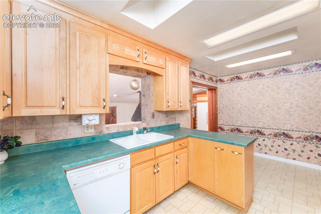 Image 10 of 29: Natural wood cabinetry, a pass-through opening, a dual basin sink, and a di