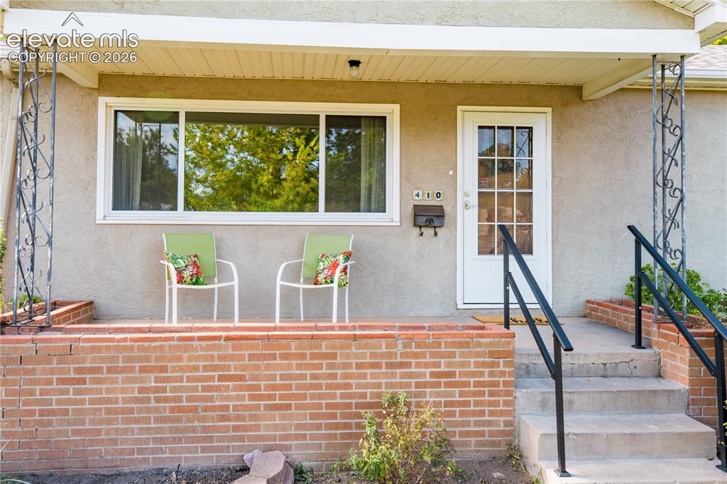 Image 2 of 29: Front porch with brick-faced half-wall, stucco exterior, and white-framed w