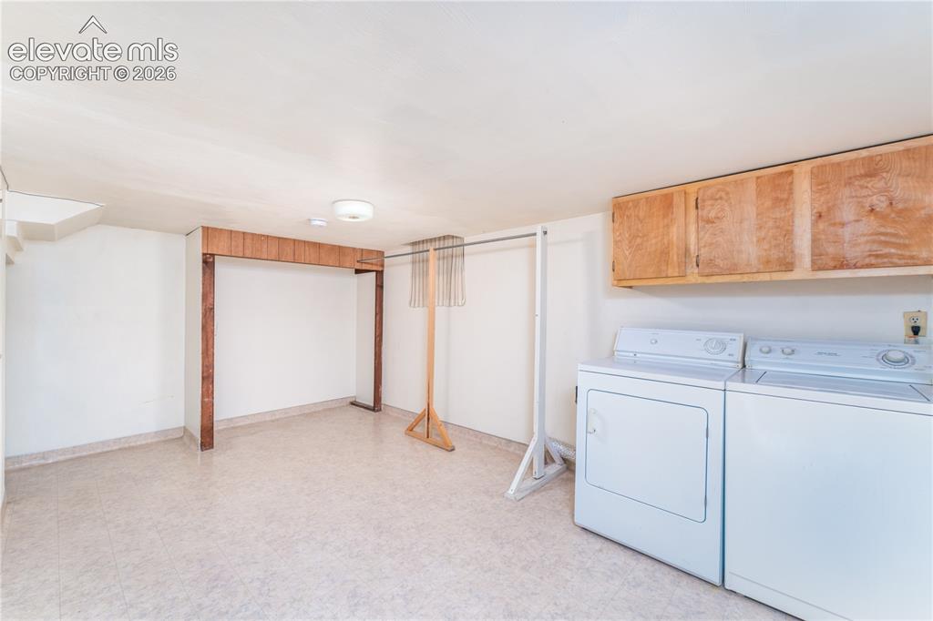 Image 21 of 29: Dedicated laundry space with light-toned flooring, overhead wood-finish cab