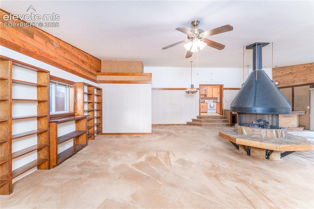 Image 7 of 29: Spacious room featuring a central fireplace with a stone hearth, extensive 