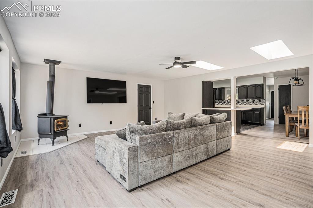 Image 21 of 35: Living room with a skylight, light wood-style flooring, a wood stove, and c