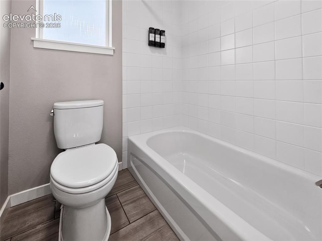 Image 27 of 50: Full bathtub with white subway tile surround, wood-finish flooring, and a p