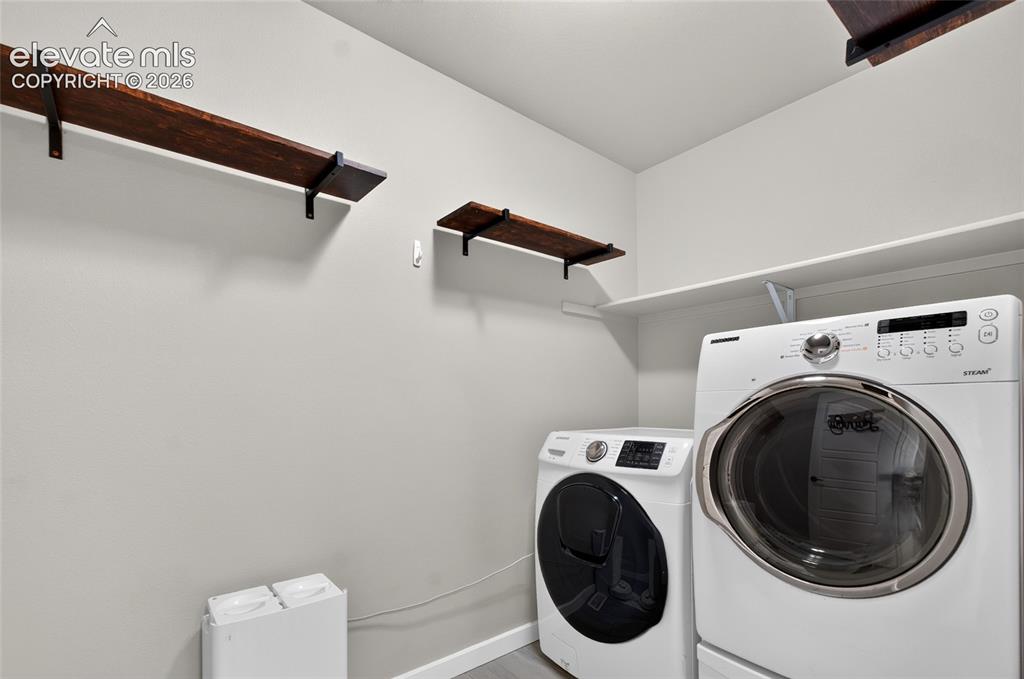 Image 30 of 50: Dedicated laundry area with a white shelving unit, wood-finish wall shelves