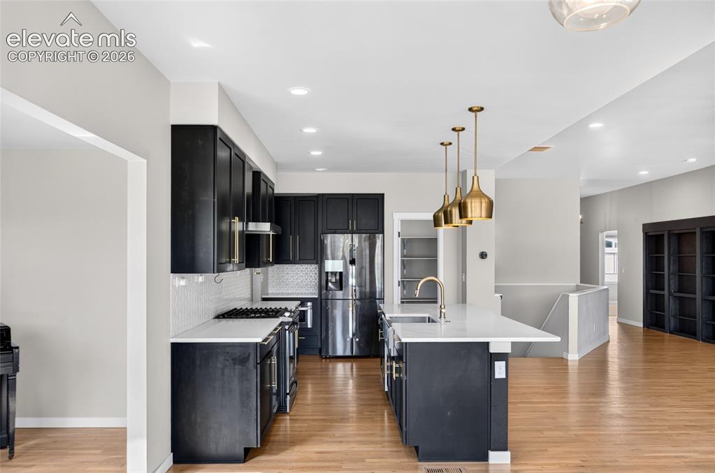 Image 8 of 50: Modern kitchen featuring dark cabinetry, white countertops, a tiled backspl