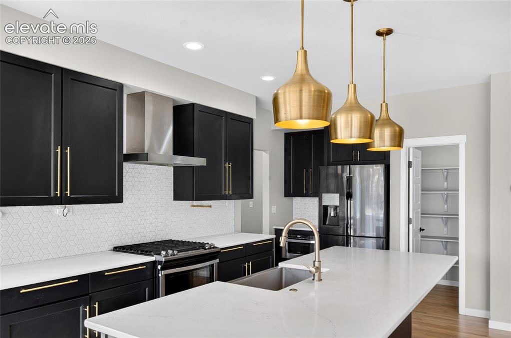 Image 9 of 50: Kitchen featuring black cabinetry with gold-finish hardware, stainless stee