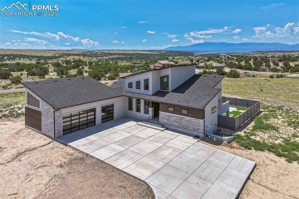 Caption: Modern home with concrete driveway, a garage, a mountain view, a shingled roof, and stone siding