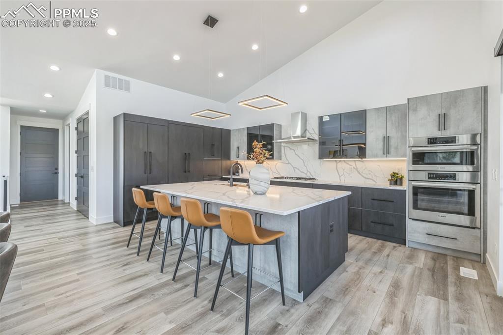 Image 13 of 50: Kitchen featuring modern cabinets, gray cabinetry, a large island, high vau