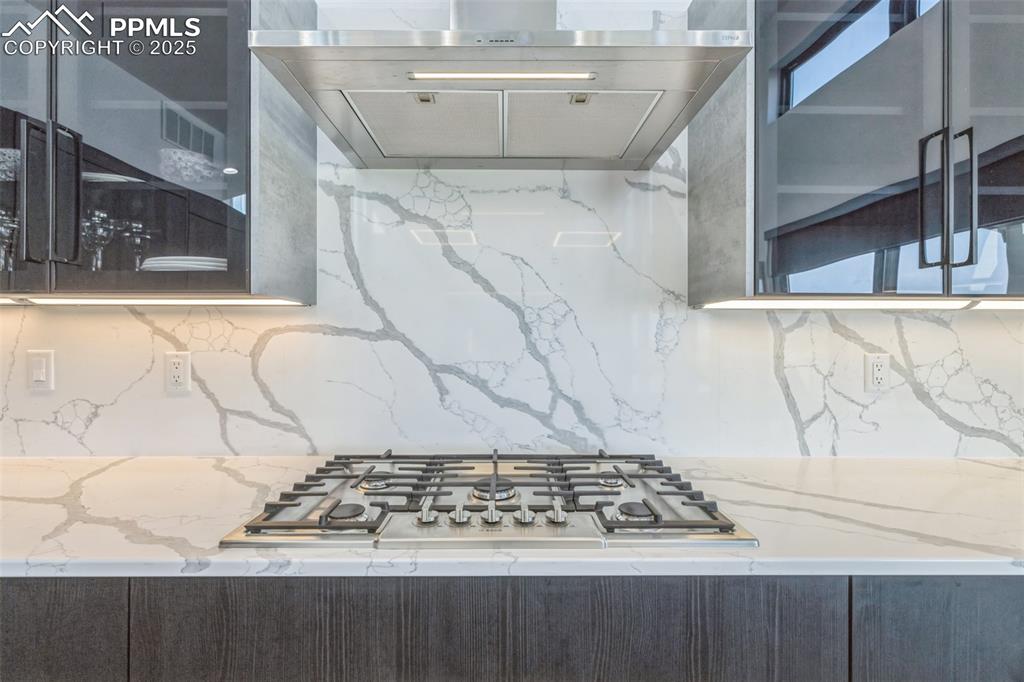 Image 15 of 50: Kitchen with exhaust hood, stainless steel gas cooktop, glass insert cabine