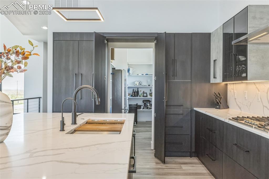 Image 17 of 50: Kitchen with modern cabinets, wall chimney exhaust hood, light stone counte