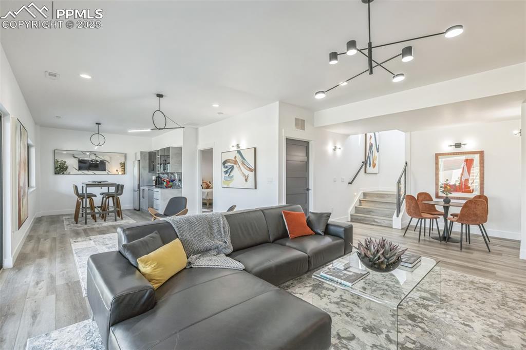 Image 22 of 50: Living area featuring stairway, light wood-style floors, a chandelier, plen