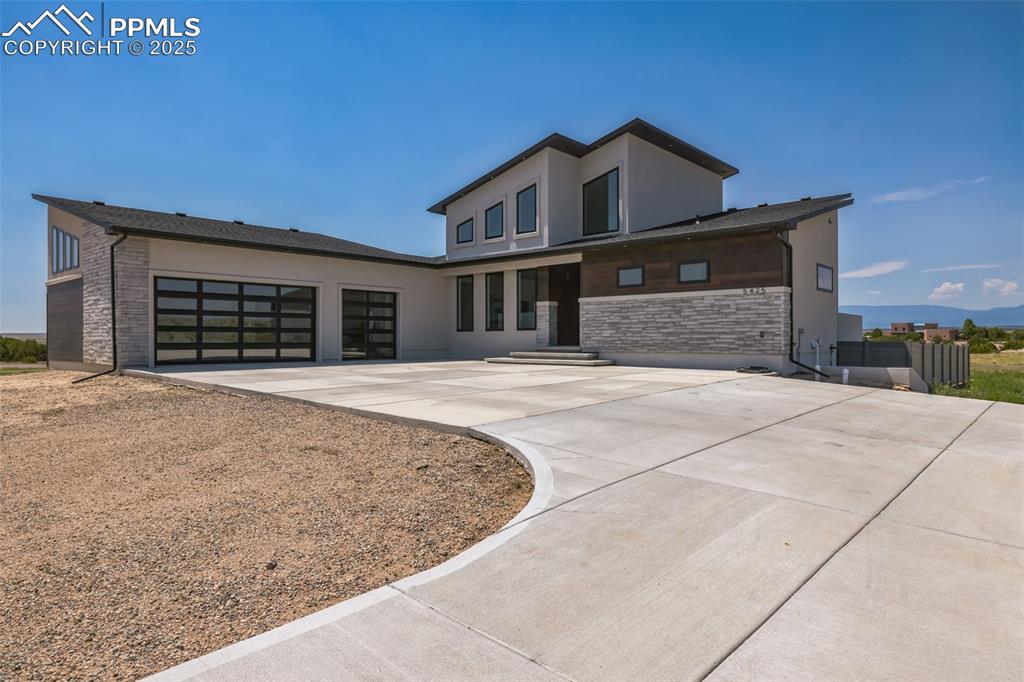 Image 3 of 50: Modern home with driveway, a garage, stucco siding, and stone siding