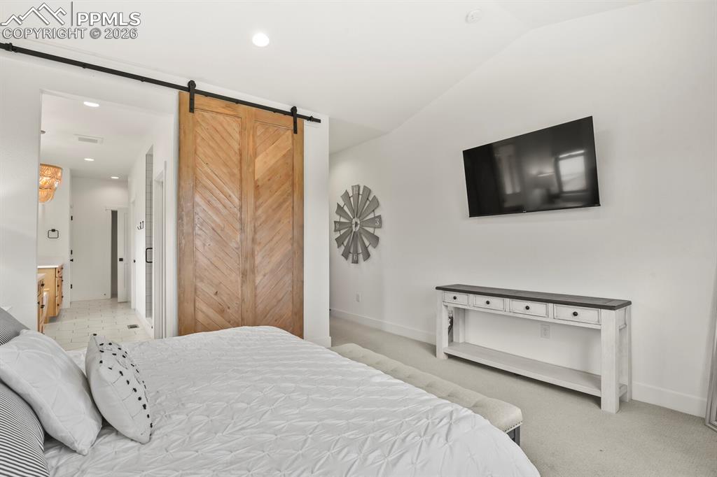 Image 20 of 47: Bedroom with a barn door, recessed lighting, vaulted ceiling, light carpet,