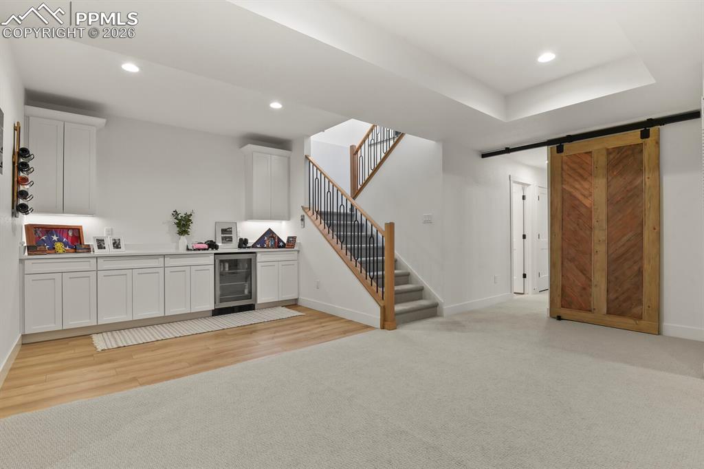 Image 32 of 47: Indoor bar featuring white cabinetry, a barn door, wine cooler, light count