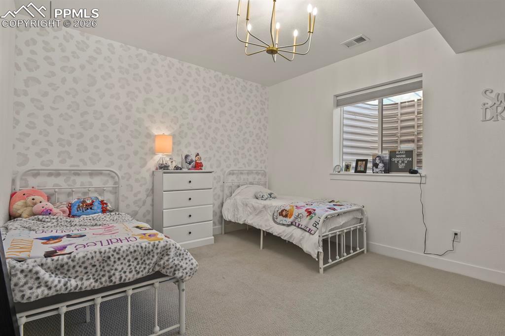 Image 36 of 47: Bedroom with hanging lights, light colored carpet, and wallpapered walls