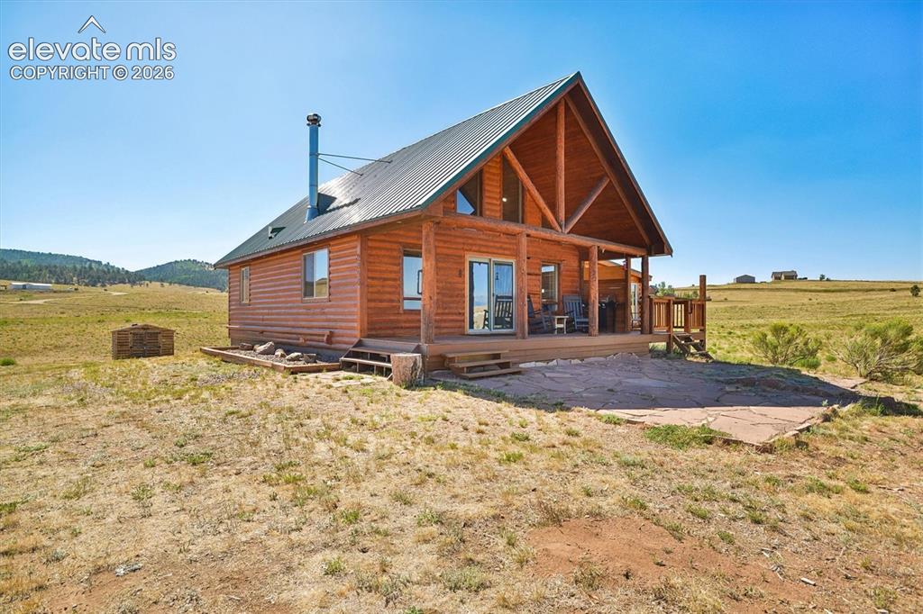 Caption: Log cabin exterior featuring a metal roof, prominent chimney, and a covered porch