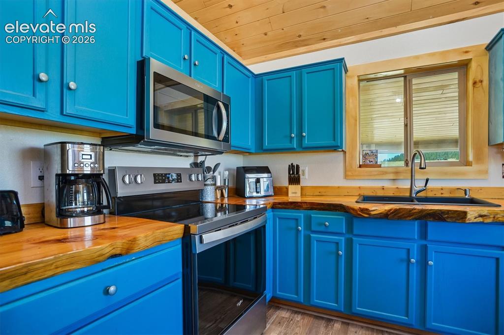 Image 8 of 29: Kitchen showcasing vibrant blue cabinetry, live-edge wood countertops, and