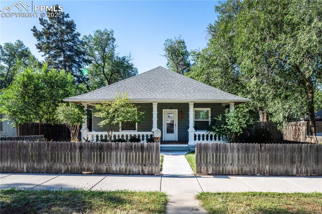 Caption: Bungalow with roof with shingles, covered porch, and a fenced front yard