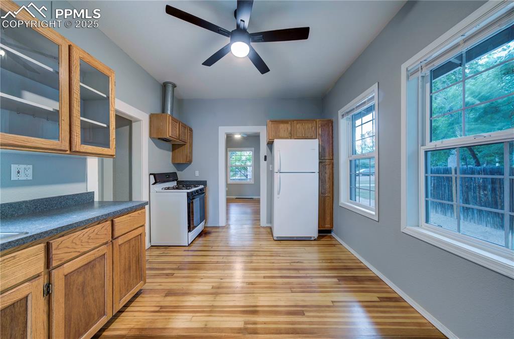 Image 10 of 19: Kitchen with glass insert cabinets, white appliances, brown cabinetry, dark