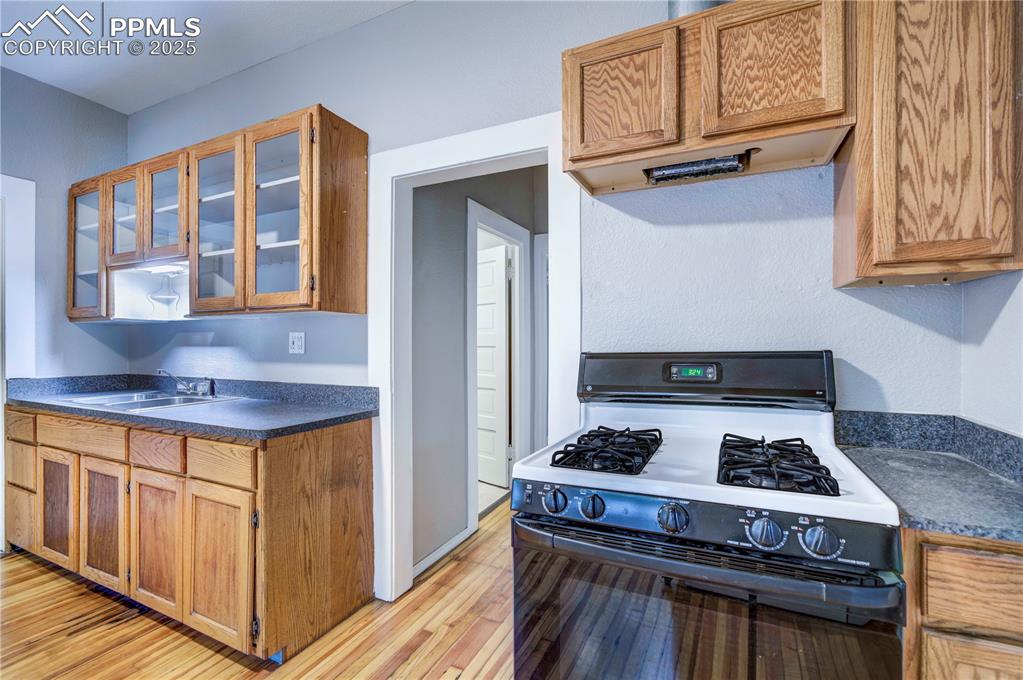 Image 11 of 19: Kitchen featuring range with gas stovetop, dark countertops, brown cabinetr