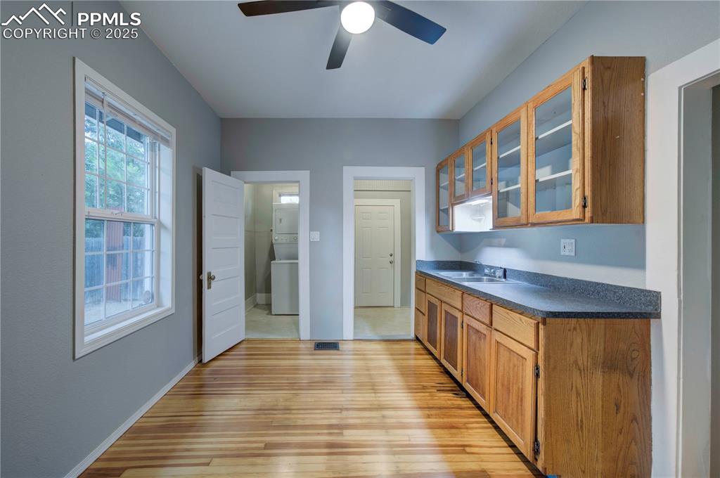 Image 13 of 19: Kitchen with glass insert cabinets, brown cabinets, dark countertops, light