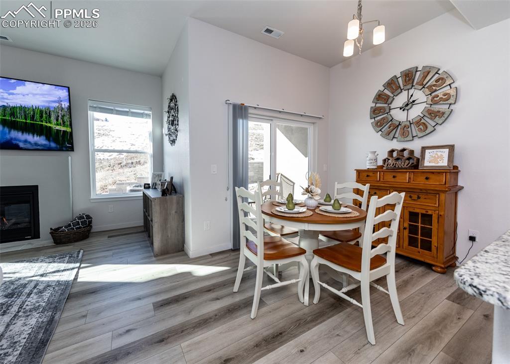 Image 19 of 49: Dining area with light wood finished floors, hanging lights, and a glass co