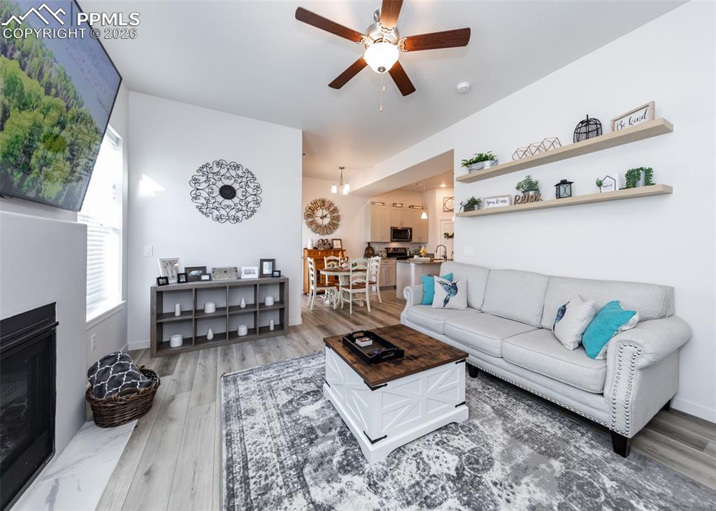 Image 21 of 49: Living room with a ceiling fan, a fireplace, and light wood finished floors