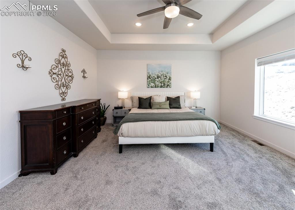 Image 25 of 49: Bedroom with a raised ceiling, light carpet, ceiling fan, and recessed ligh