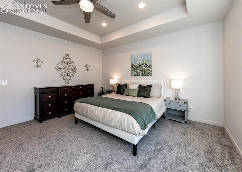Image 27 of 49: Bedroom with a raised ceiling, carpet floors, ceiling fan, and recessed lig