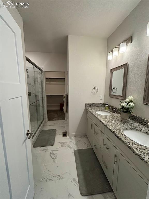 Image 29 of 49: Bathroom with a spacious closet, double vanity, a shower stall, light marbl