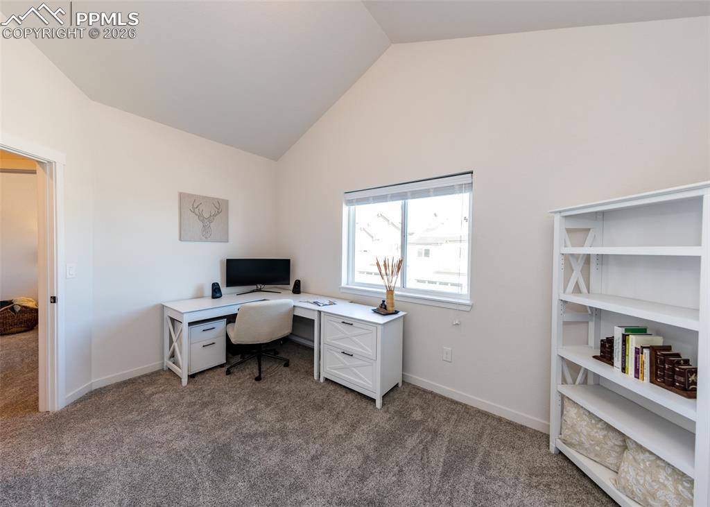 Image 39 of 49: Office with dark carpet and lofted ceiling