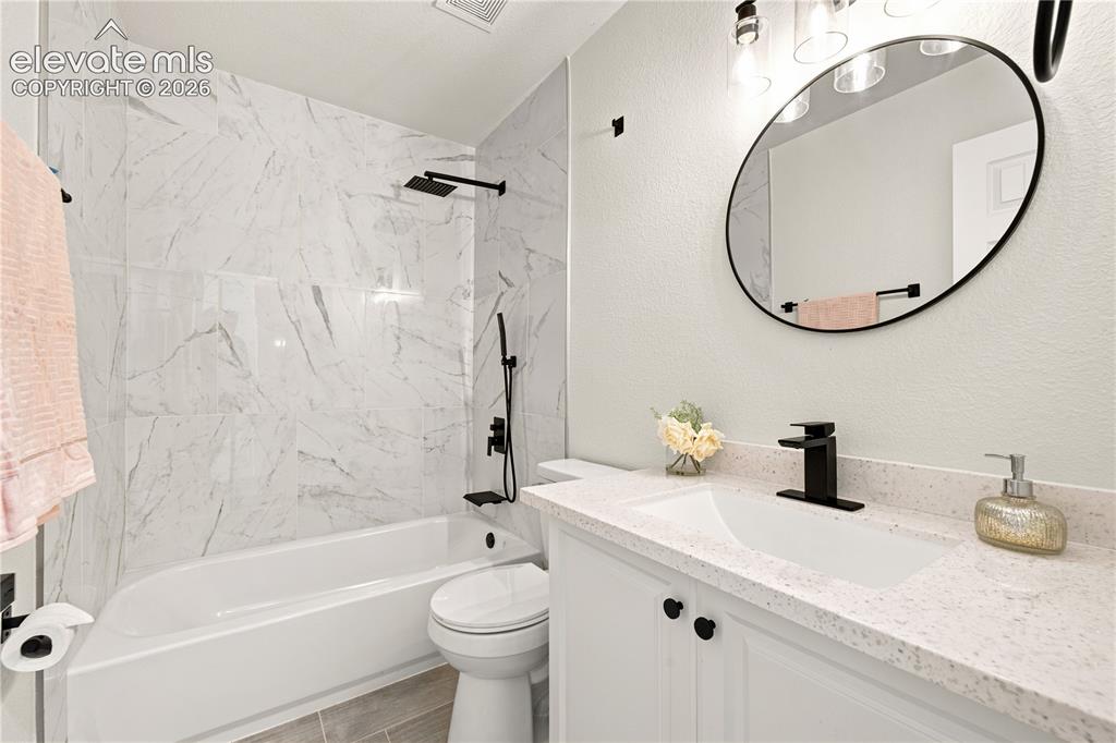 Image 16 of 40: Bathroom featuring a white bathtub with a tile surround, black rainfall sho
