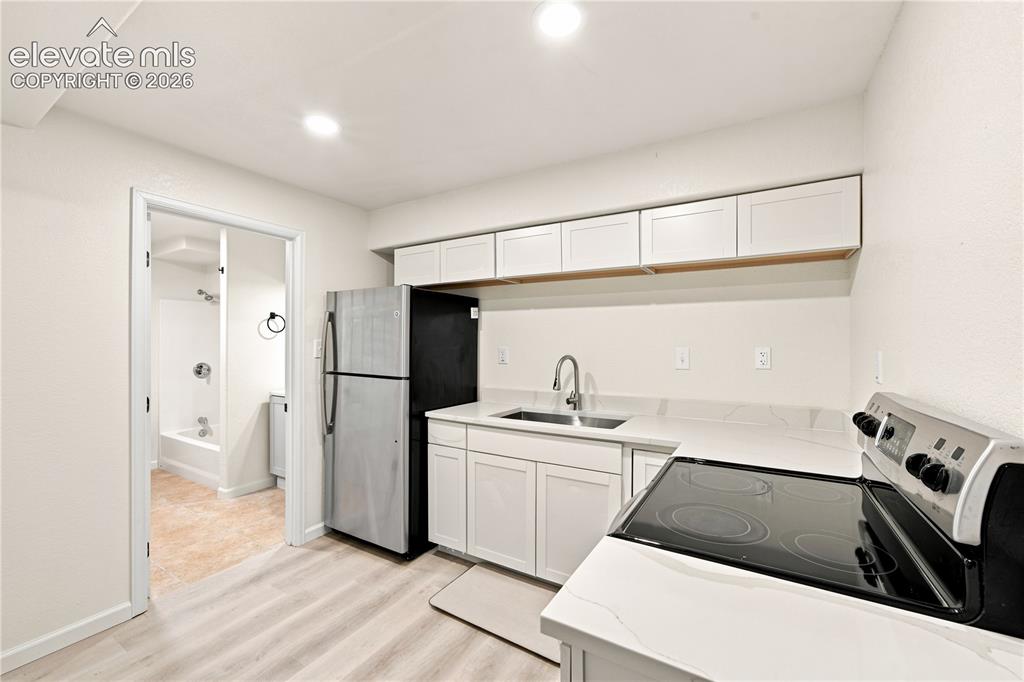 Image 28 of 40: Compact kitchen area featuring wood-finish flooring, white cabinetry, integ