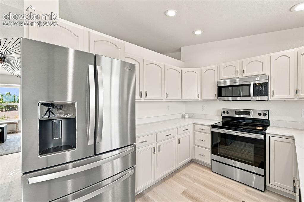 Image 4 of 40: Modern kitchen featuring white cabinetry, light-toned countertops, and stai