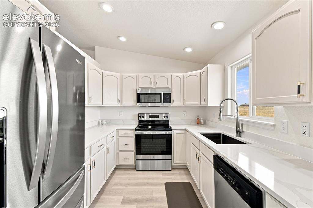 Image 5 of 40: U-shaped kitchen with light wood-finish flooring, white cabinetry, stainles
