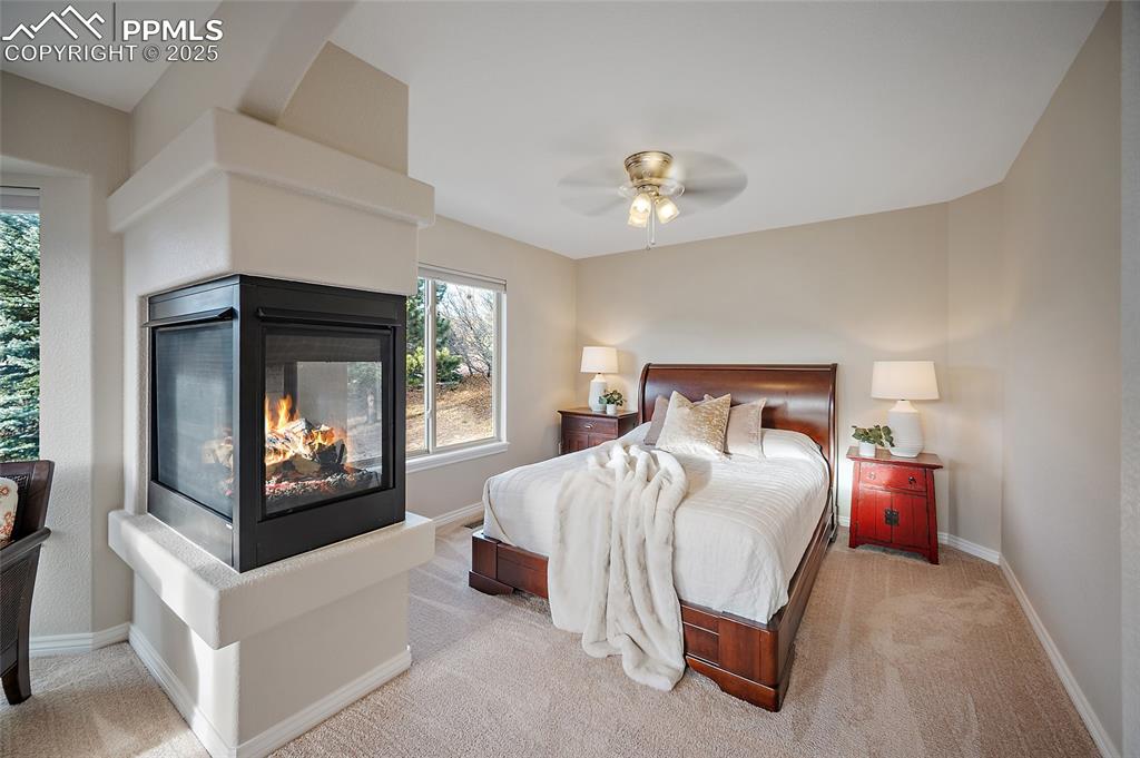 Image 23 of 50: Bedroom with a multi sided fireplace, light colored carpet, and a ceiling f
