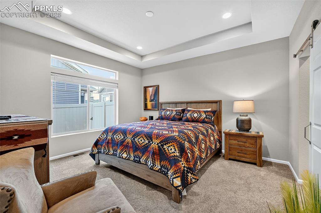 Image 18 of 43: Bedroom featuring a raised ceiling, carpet, a barn door, and recessed light