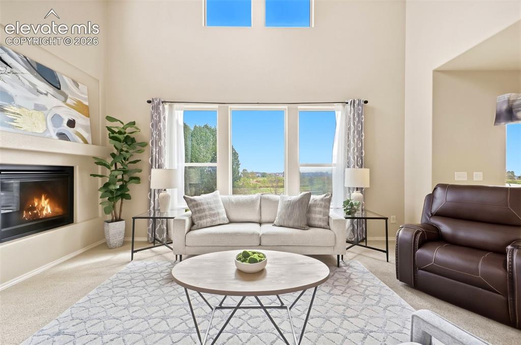 Image 12 of 40: Open living room with high ceilings, tons of natural light, and a gas firep