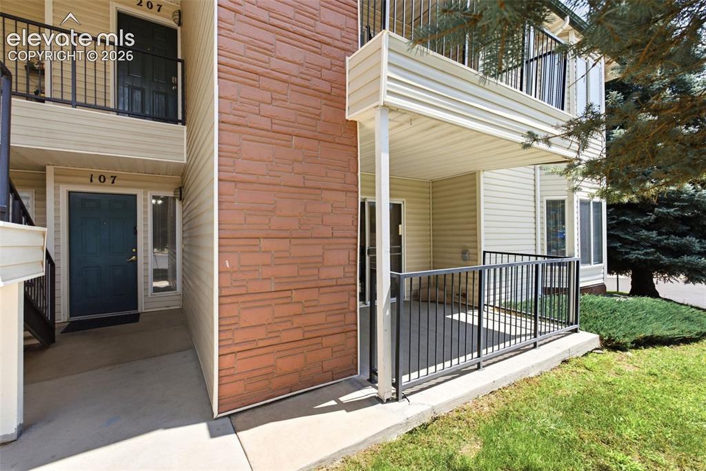 Image 2 of 25: Ground-level patio with black metal railing, adjacent to a textured stone f