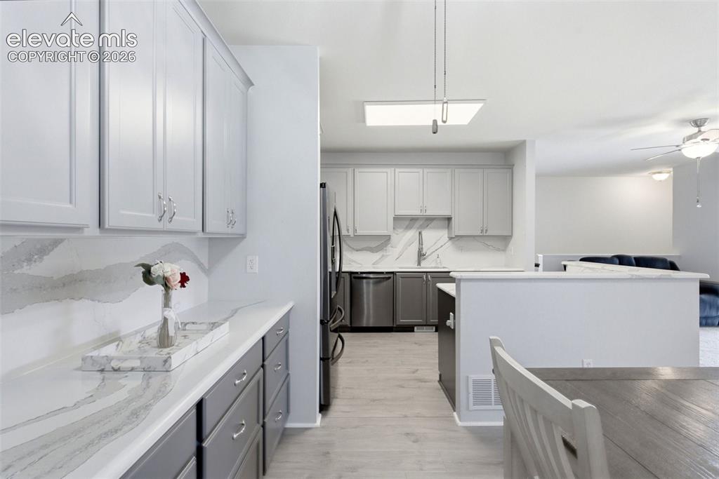 Image 9 of 25: White shaker-style upper cabinetry with stainless steel hardware, gray lowe