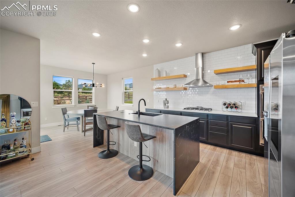 Image 16 of 46: Kitchen featuring a kitchen island with sink, a breakfast bar, tasteful bac